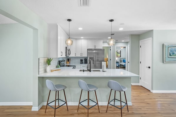 Une cuisine moderne dotée d’un îlot central, de tabourets de bar, d’appareils électroménagers en acier inoxydable et de luminaires suspendus.