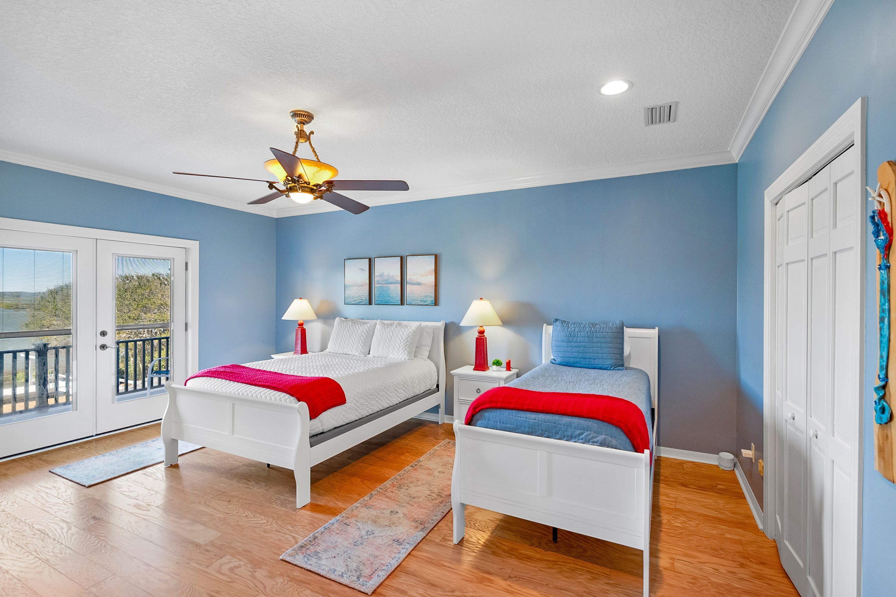 A bedroom with two beds, a ceiling fan, and a view through a sliding glass door.