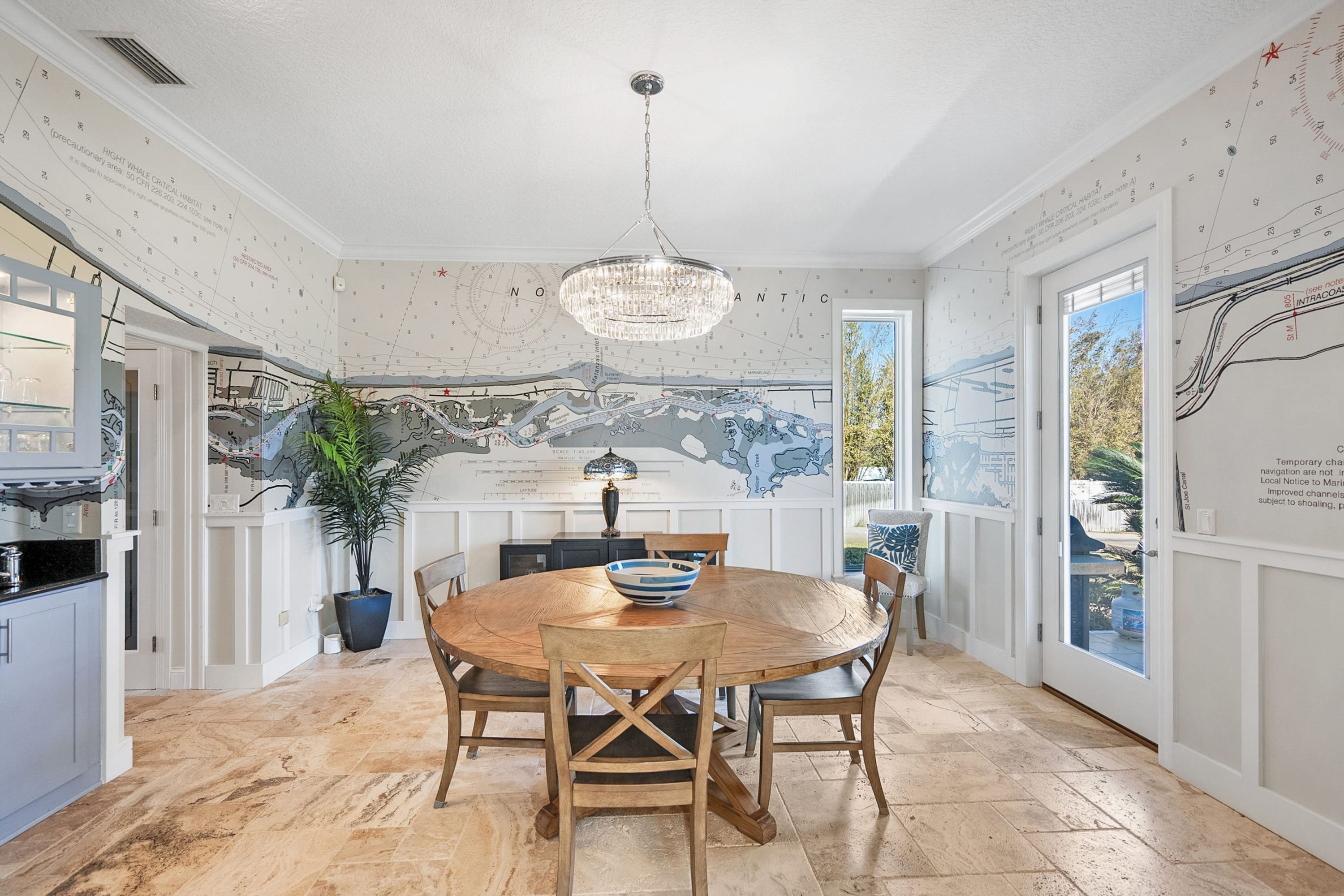 A dining area with a round wooden table, chairs, a chandelier, and a large potted plant.