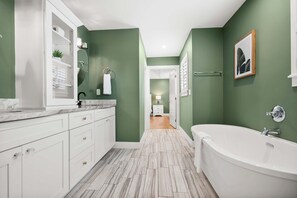 Un baño moderno con una bañera independiente, muebles blancos y una pared de acento verde.
