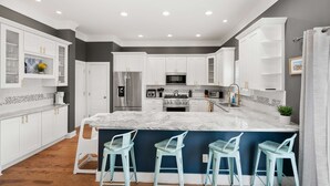 A modern kitchen with white cabinets, a marble island, and three bar stools. - Magnolia Ave Downtown By Beach Kids Playset (St. Augustine)