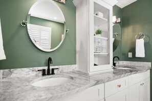 Un baño con un lavabo blanco, un espejo redondo y un mueble blanco con un estante.