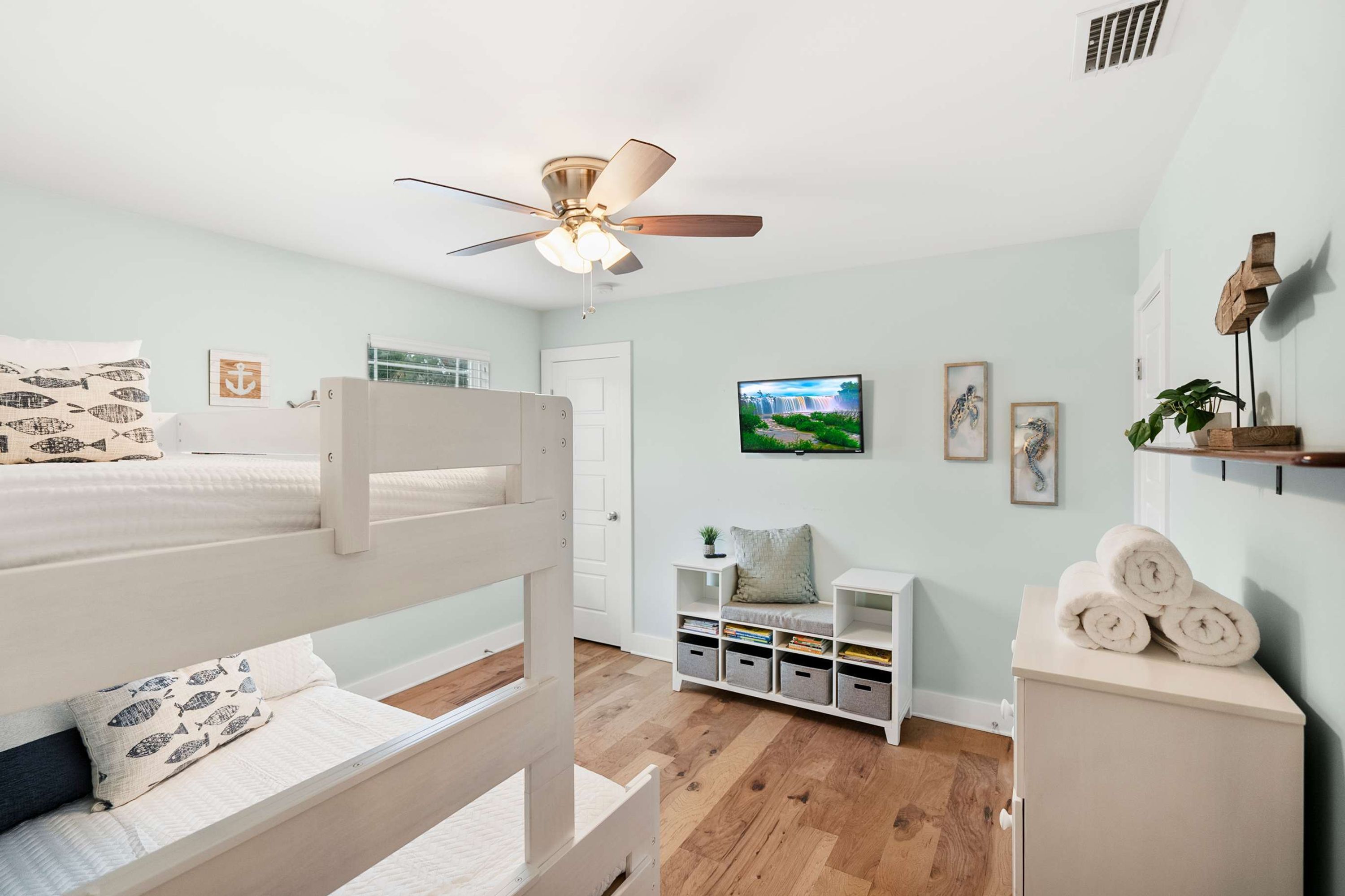A bedroom with a bunk bed, a ceiling fan, a TV, a bookshelf, and a small plant.