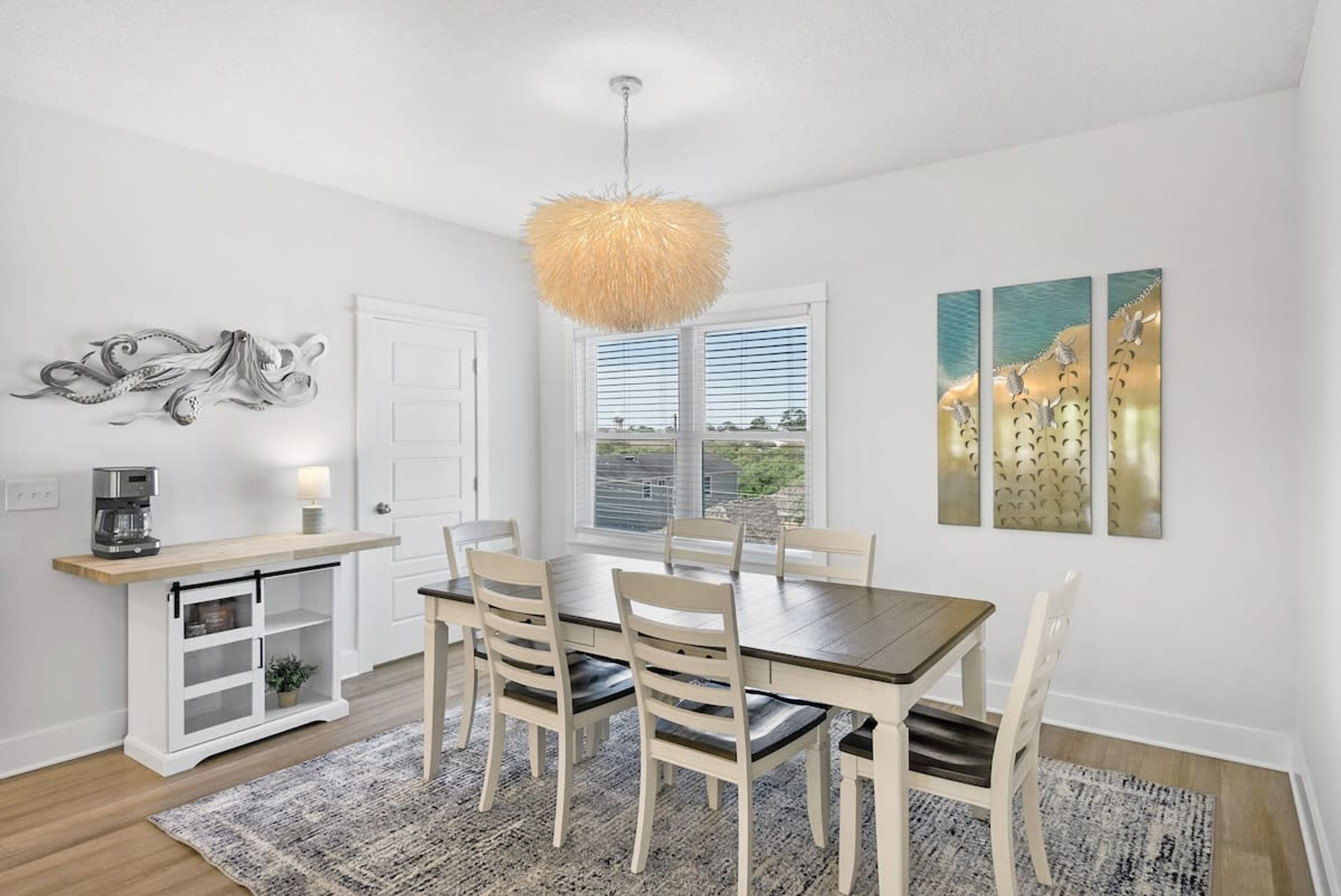 A dining area with a wooden table, white chairs, a hanging light fixture, and artwork on the wall.