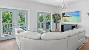 Una sala de estar con un sofá blanco, un televisor de pantalla plana y un ventanal con vistas a la vegetación y una playa.