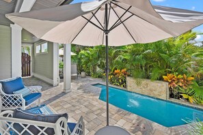 Un espace aménagé au bord de la piscine, comprenant un coin salon couvert, une piscine et une végétation tropicale luxuriante.