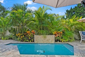 Une piscine entourée d’une végétation tropicale luxuriante et une terrasse carrelée.
