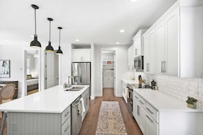 Une cuisine moderne avec des meubles blancs, un îlot central, des luminaires suspendus et un tapis à motifs.