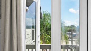 Puerta abierta que da a un balcón con vistas a un autobús estacionado y vegetación.