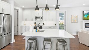 Una cocina moderna con armarios blancos, electrodomésticos de acero inoxidable y una isla central con taburetes de bar.