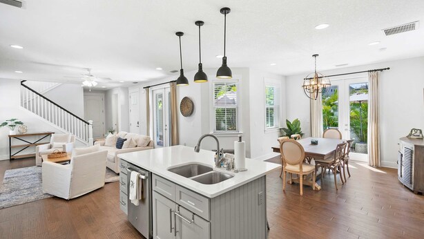 Una cocina moderna con una isla central, un comedor con sillas de madera y una escalera que sube a otro nivel.