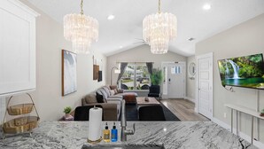 A modern living room with a marble countertop, chandelier, and a large TV. - 5 Minutes to Beach and Downtown Fire pit Grill (St. Augustine)