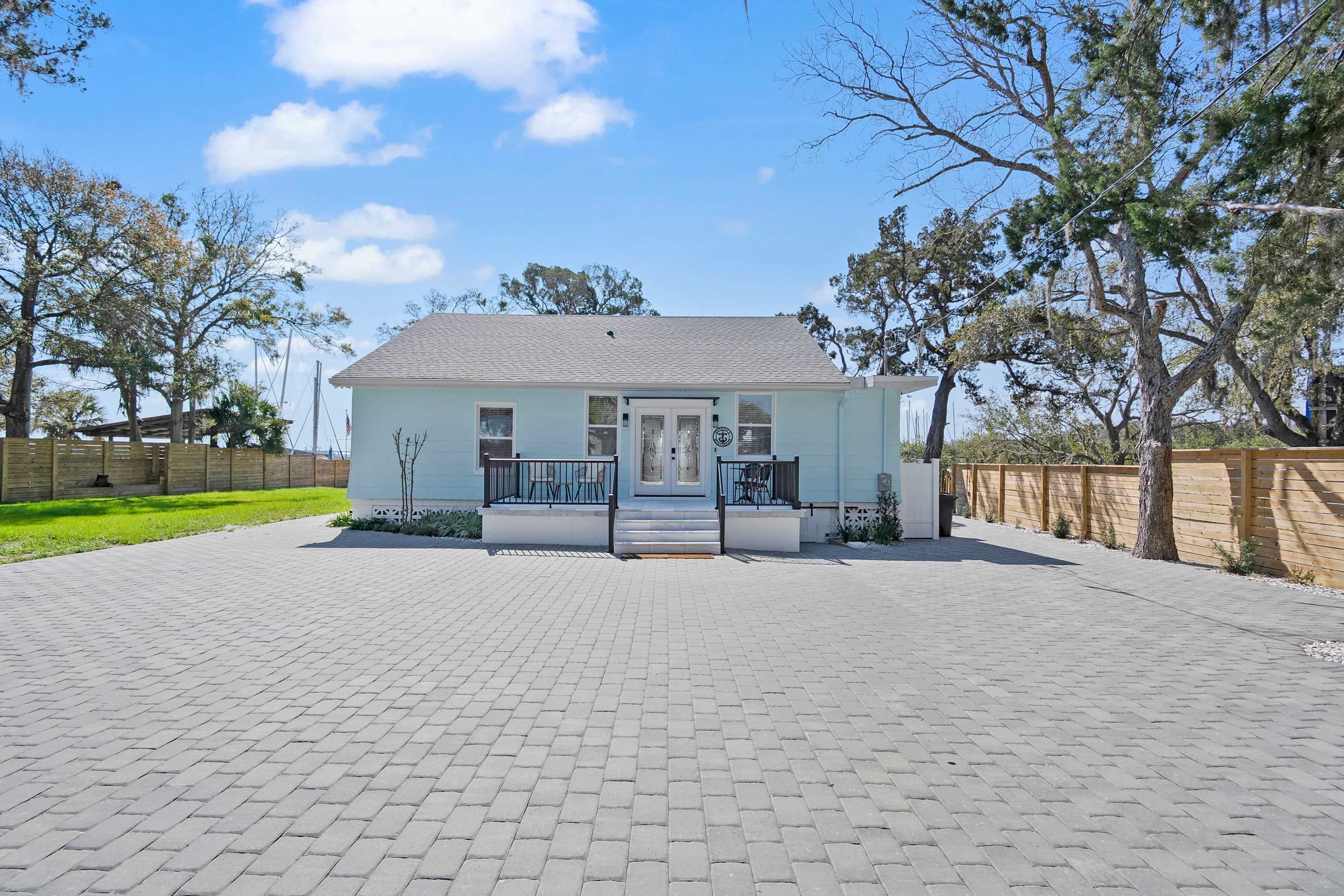 A light blue house with a grey roof, a front porch with a railing, and a paved driveway.