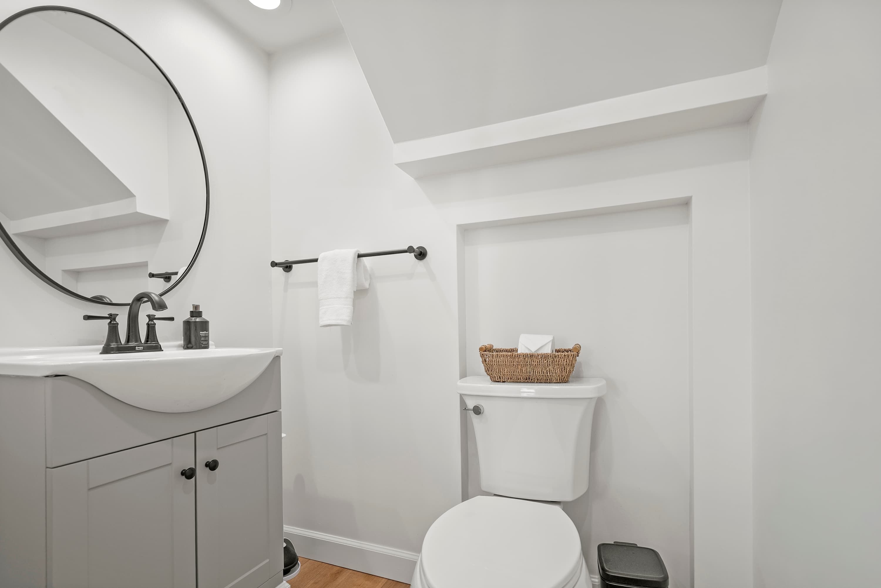 A modern bathroom with a white sink, a large mirror, a toilet, and a small trash bin.