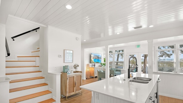 A modern kitchen with white cabinetry, a wooden staircase, and a large window offering a view of the outdoors. - Waterfront Incredible Views Fire pit Renovated (St. Augustine)