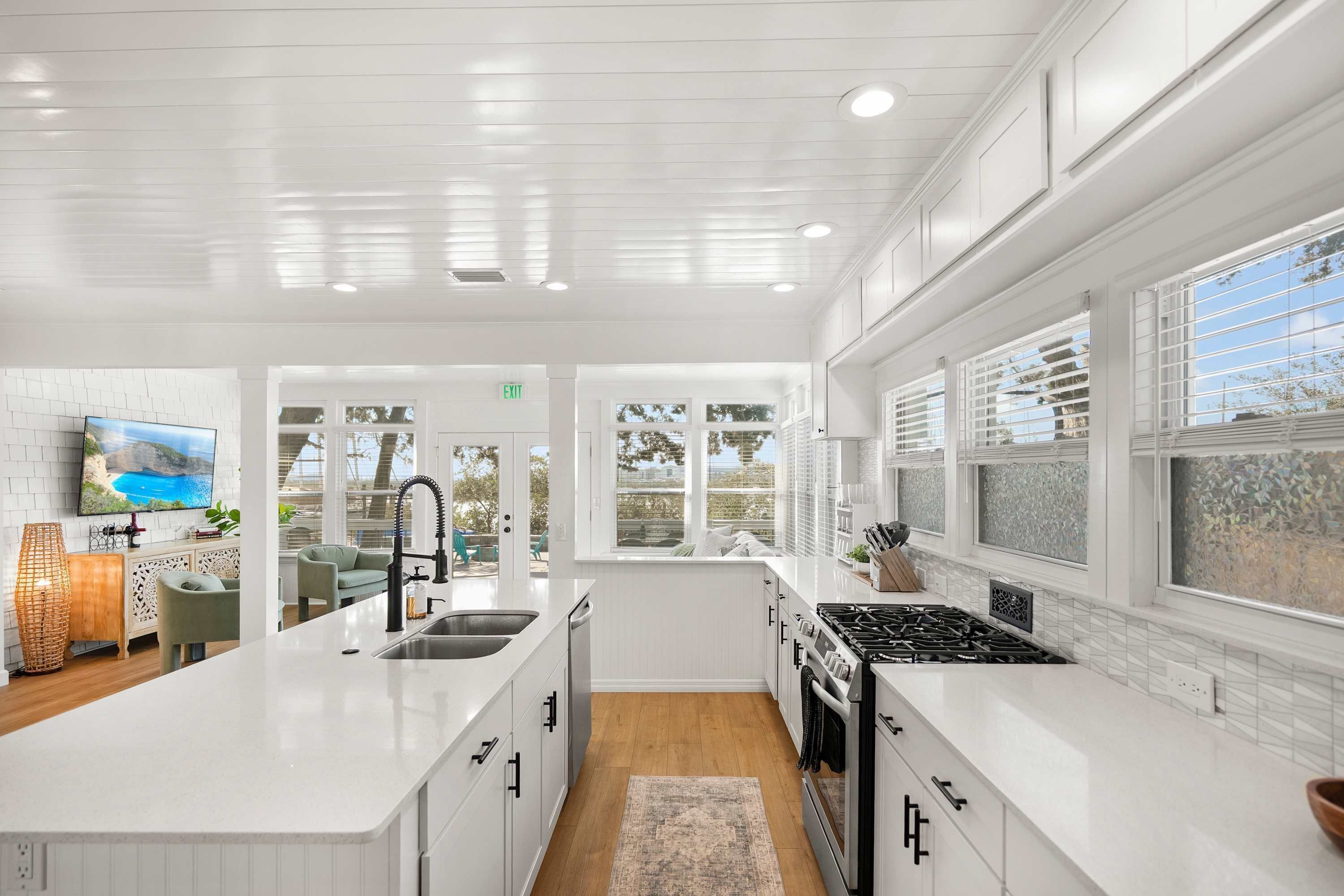 A modern kitchen with white cabinetry, a central island, and a large window providing a view of the outdoors.