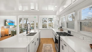 A modern kitchen with white cabinetry, a central island, and a large window providing a view of the outdoors. - Waterfront Incredible Views Fire pit Renovated (St. Augustine)