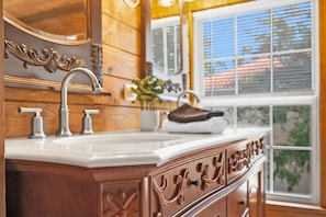 A wooden bathroom vanity with a white countertop, a large mirror, and a window with blinds. - Historic in Downtown St Aug Steps to Ice Plant (St. Augustine)