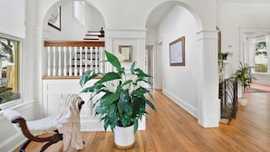A hallway with a wooden bench, a large potted plant, and a staircase with white railings. - Historic in Downtown St Aug Steps to Ice Plant (St. Augustine)