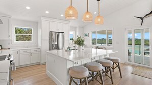 Une cuisine spacieuse avec des meubles blancs, un grand îlot central doté de tabourets et un éclairage suspendu.