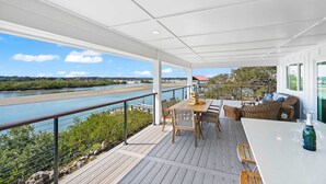 Un espace extérieur abrité, doté d’une terrasse en bois, d’une table avec des chaises et offrant une vue sur une rivière.