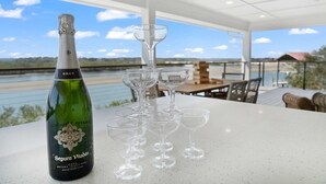 Une bouteille de vin brut et plusieurs verres à vin sont posés sur une table, avec en arrière-plan une vue sur une rivière et un bâtiment.