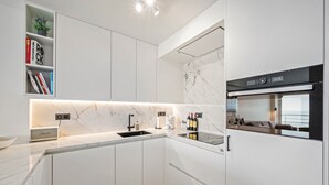 Μια μοντέρνα κουζίνα με λευκά ντουλάπια, πάγκο από μάρμαρο, εντοιχισμένο φούρνο και ράφι για κρασιά.