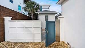 A modern residential area with a white garage, a blue gate, and a wooden fence. - 100 Steps to Beach Deck w Ocean View Beach Gear (St. Augustine)