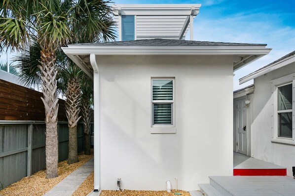 A small, single-story house with a white exterior, a window with shutters, and a red step leading to the front door. - 100 Steps to Beach Deck w Ocean View Beach Gear (St. Augustine)