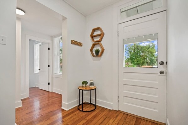 A hallway with wooden flooring, a white door with a window, and a small round table with a plant and a lamp. - Stay in A Castle In St Augustine Hot Tub Fireplace (St. Augustine)