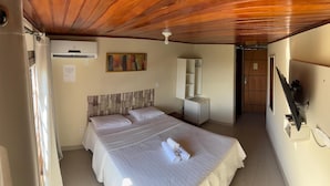 A hotel room with a wooden ceiling, a bed with white bedding, a bedside table, a wardrobe, and a television mounted on the wall. - Pousada Dos Atobás (Arraial do Cabo)