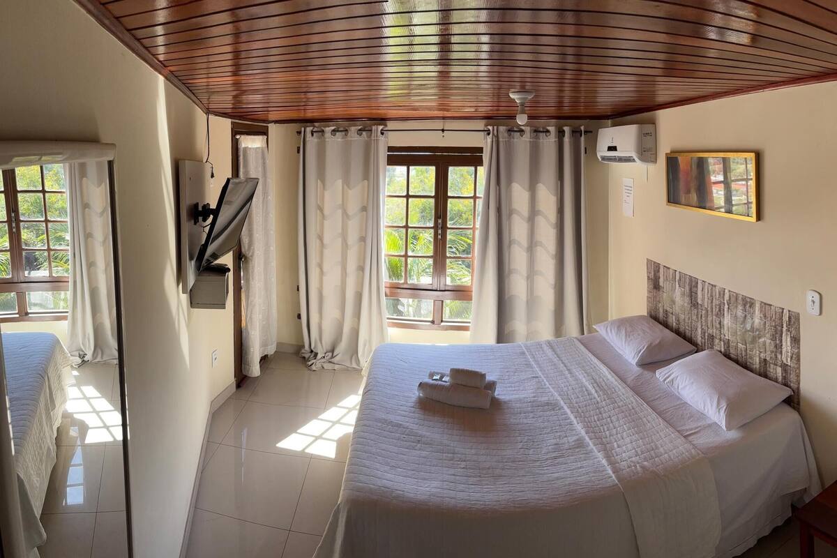 A hotel room with a large bed, a wardrobe, a desk, and a window with curtains.