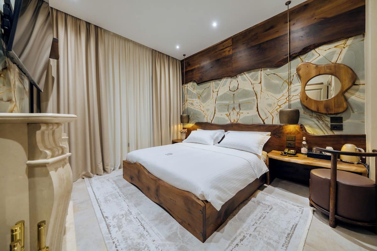 A modern bedroom with a wooden bed frame, a marble-patterned wall, and a large mirror.