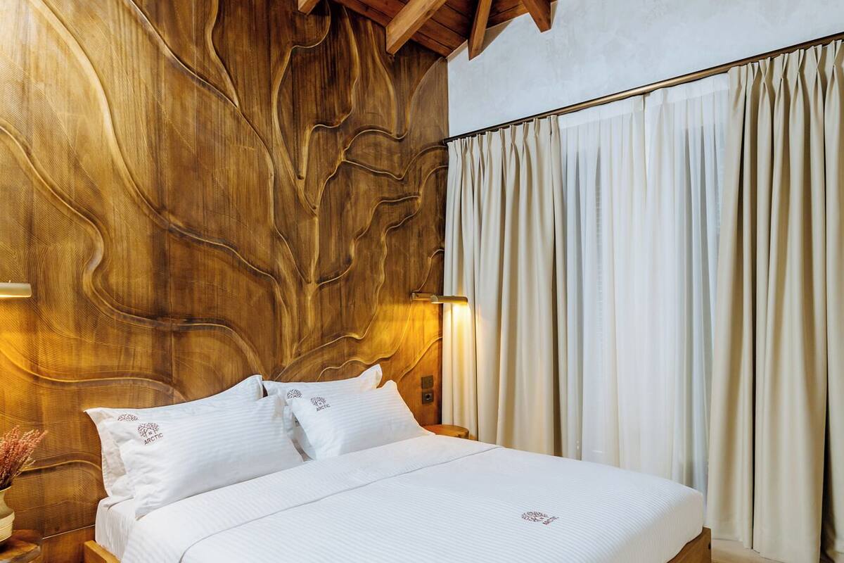 A wooden-framed bed in a room with a unique wooden wall design and a patterned rug.