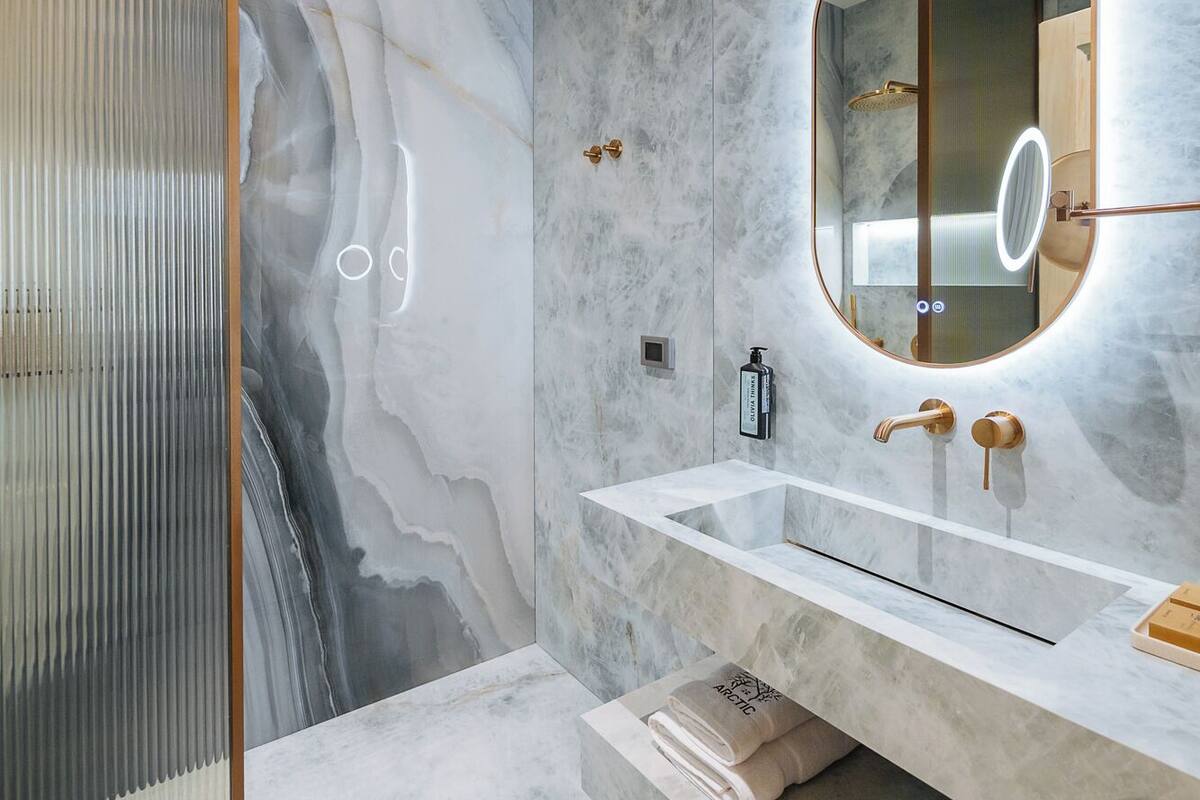 A modern bathroom with marble walls, a large mirror, and a vanity with a towel rack.