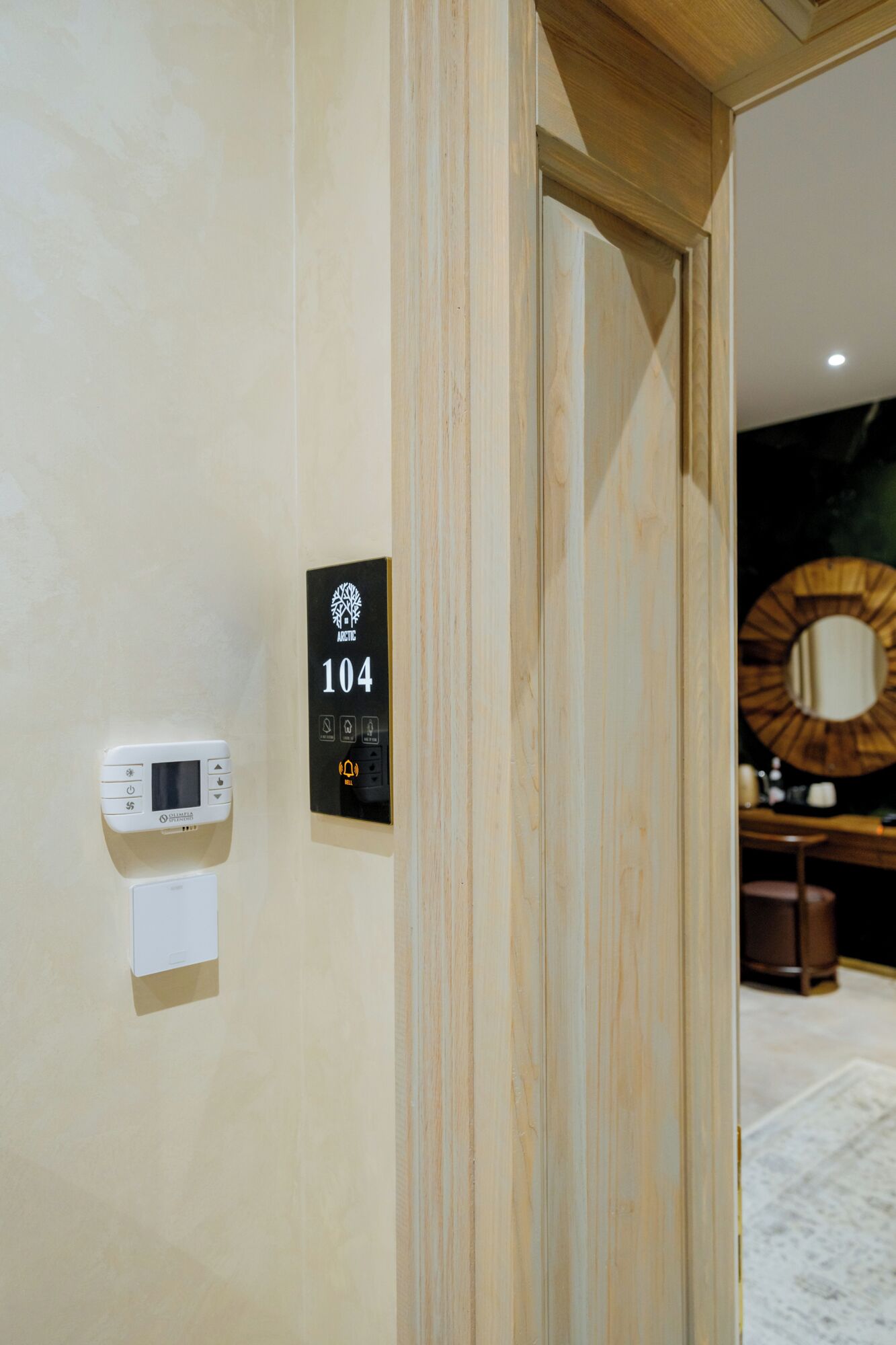 A hotel room entrance with a wooden door, a digital thermostat, and a room number sign.
