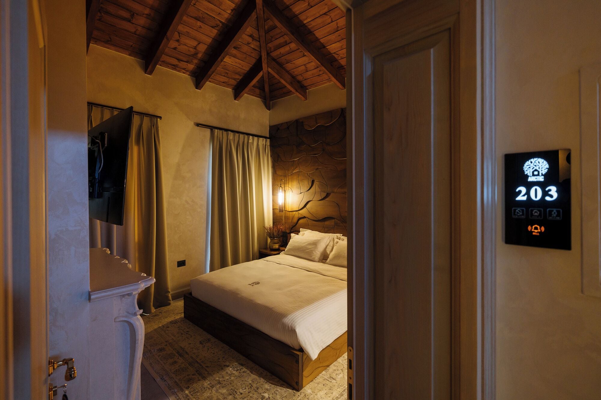 Habitación de hotel con cama, cortinas, una lámpara fijada a la pared y un cartel con el número de la habitación.