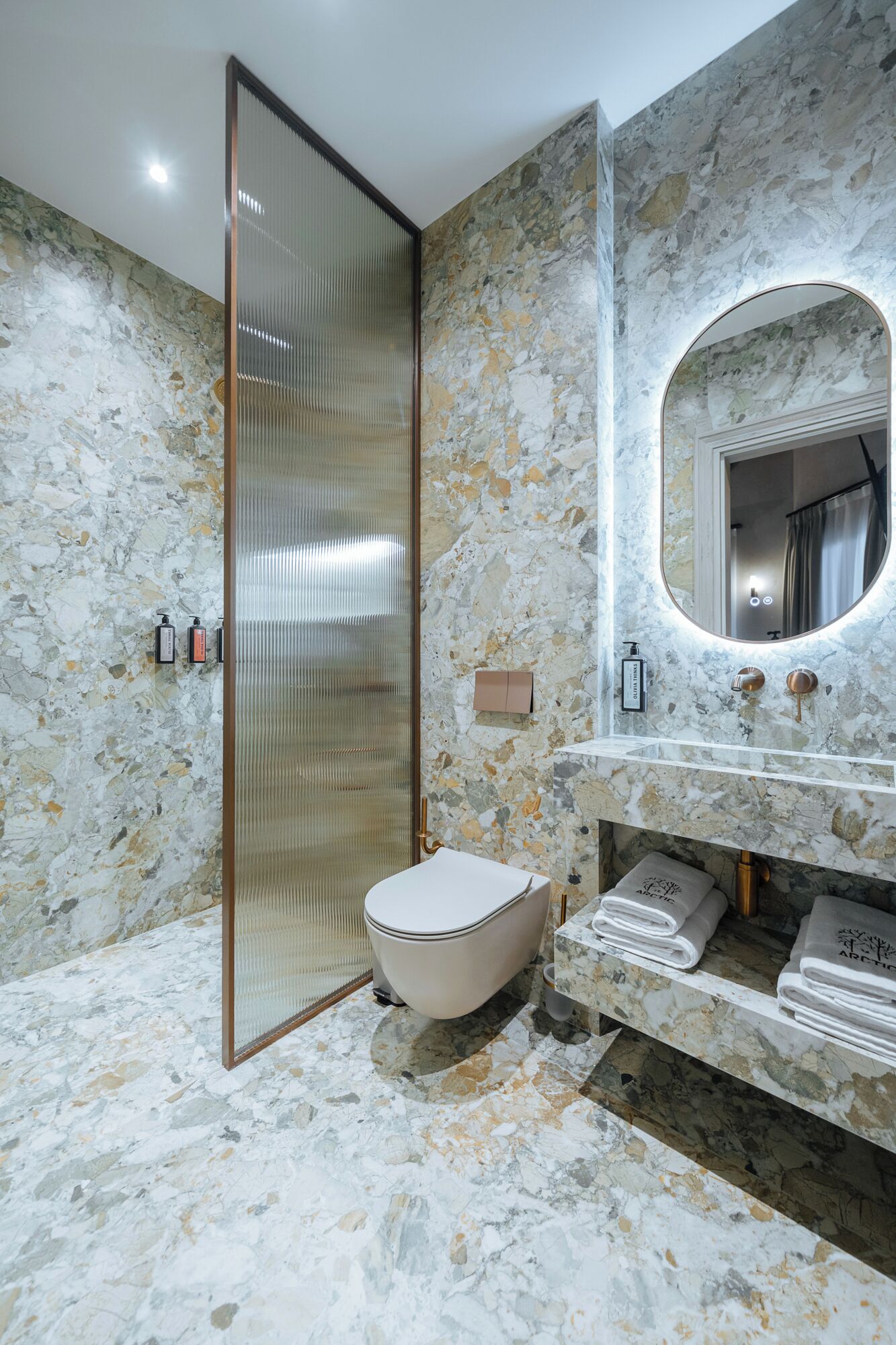 A bathroom with a marble floor, a toilet, a sink with a mirror, and a shower area.