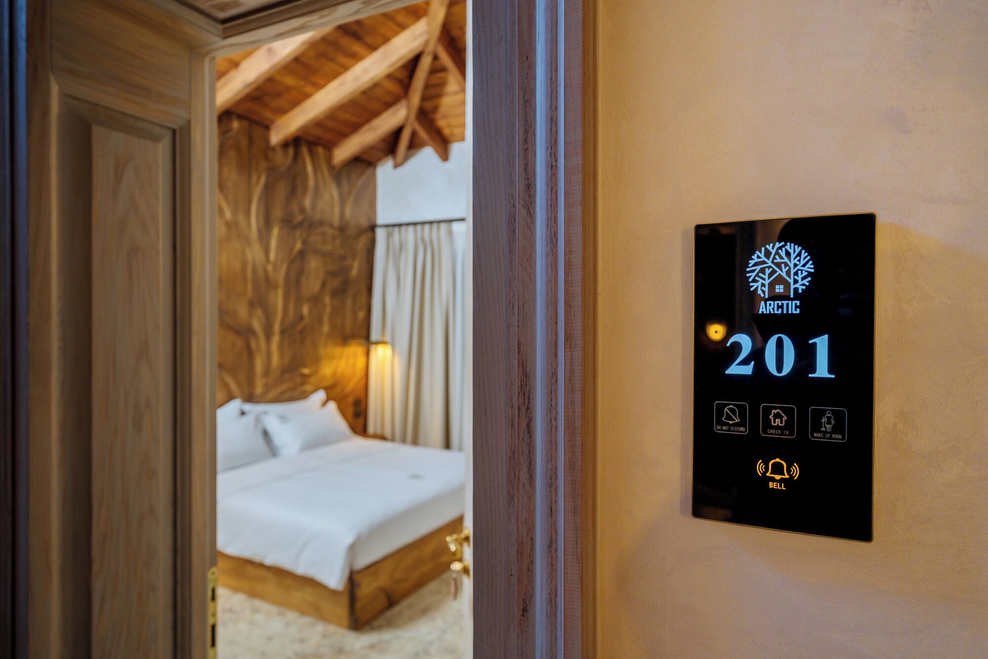 Une chambre d’hôtel avec un plafond en bois, un lit et un panneau de commande fixé au mur, affichant le numéro de chambre 201 ainsi que divers icônes de contrôle.