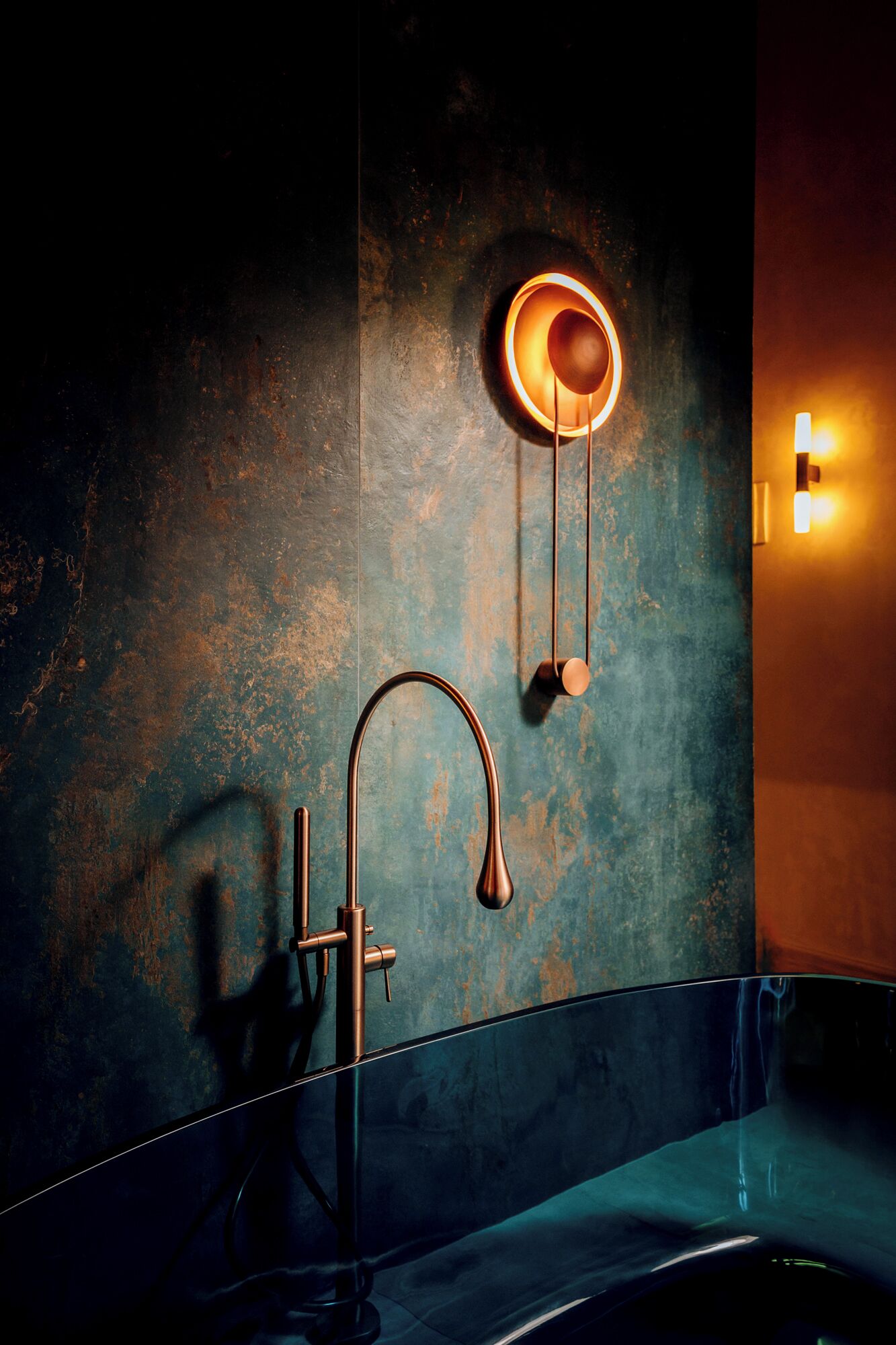 A bathroom with a modern faucet, a wall-mounted light fixture, and a textured wall.