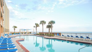 A pool area with blue lounge chairs, palm trees, and a view of the ocean. - Master on Gulf & close to Everything & Free round of Golf & Activities Daily! (Panama City Beach)