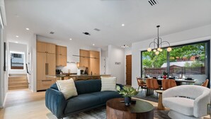 A modern kitchen with wooden cabinets, a dining area with a table and chairs, and a living room with a sofa and coffee table.