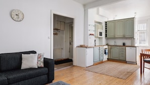 A modern kitchen with white cabinets, a microwave, and a dishwasher. There is a dark-colored sofa with a cushion and a rug on the wooden floor. - Vintage 1BR Apt in Kamppi  (Helsinki)
