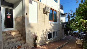 A two-story building with a brick facade, a wooden staircase, and a small outdoor seating area. - Uğur Otel (Kas)