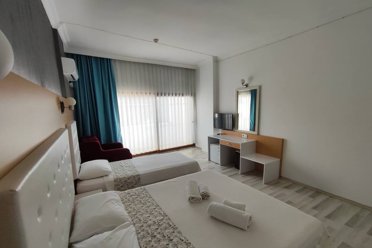 Habitación de hotel con dos camas, un escritorio, un televisor y una ventana con cortinas.
