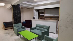 A modern living room with a green table, grey sofas, and a kitchen area in the background. - Uğur Otel (Kas)