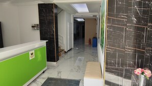 A hotel lobby with a reception desk, a green counter, a blue carpet, a white bench, and a black marble wall with a fire extinguisher. - Uğur Otel (Kas)