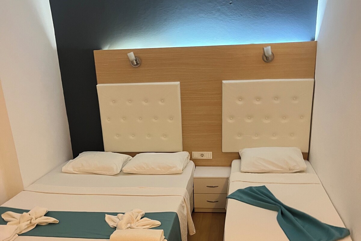 A hotel room with two single beds, a wooden headboard, a small bedside table, and a nightstand.