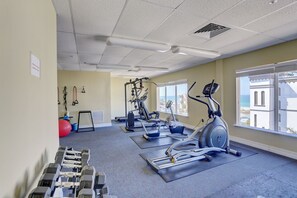 Un gimnasio con equipamiento de ejercicio, una pelota roja y vista al océano a través de amplias ventanas.