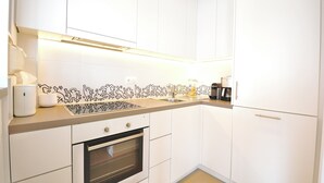 A modern kitchen with white cabinets, a built-in oven, a countertop with a coffee maker, and a patterned backsplash. - Apartment in Knokke Near the Beach (Knokke-Heist)